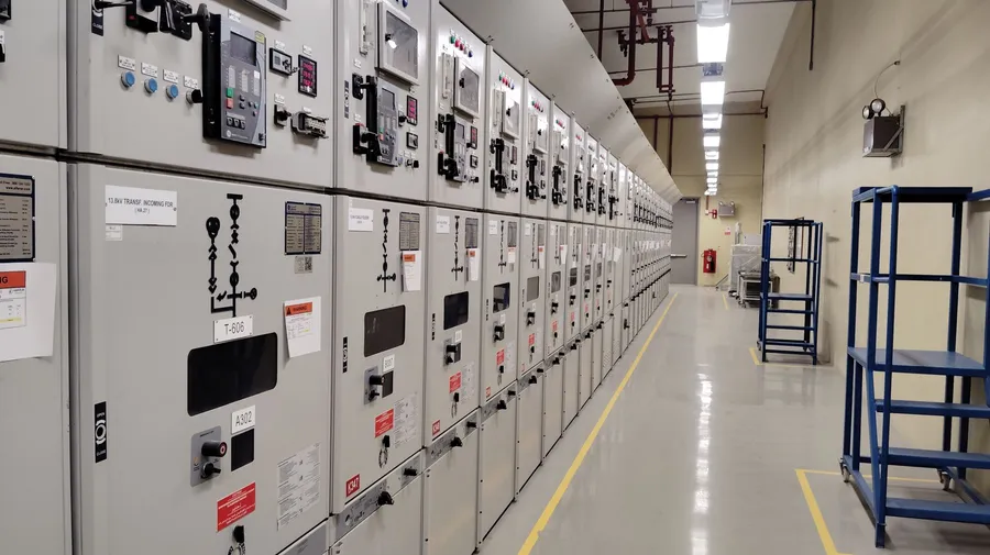 A row of electrical switchgear cabinets along a facility equipment-room aisle